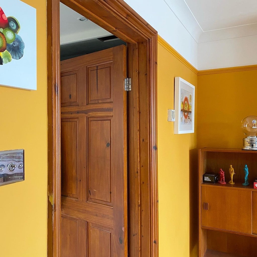 Wooden door in a room with yellow walls, a shelf with decorative items, and framed pictures.