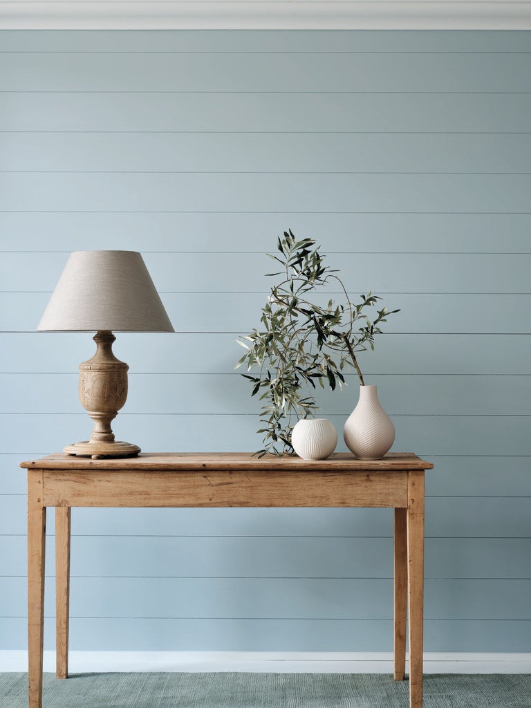 Wooden table with lamp, vase, and plant against a light blue wall