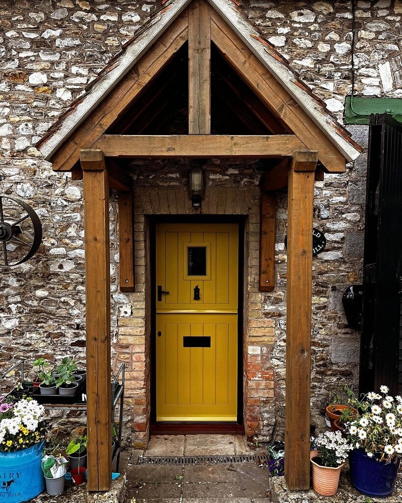 Yellow door with wooden frame in front of a stone wall