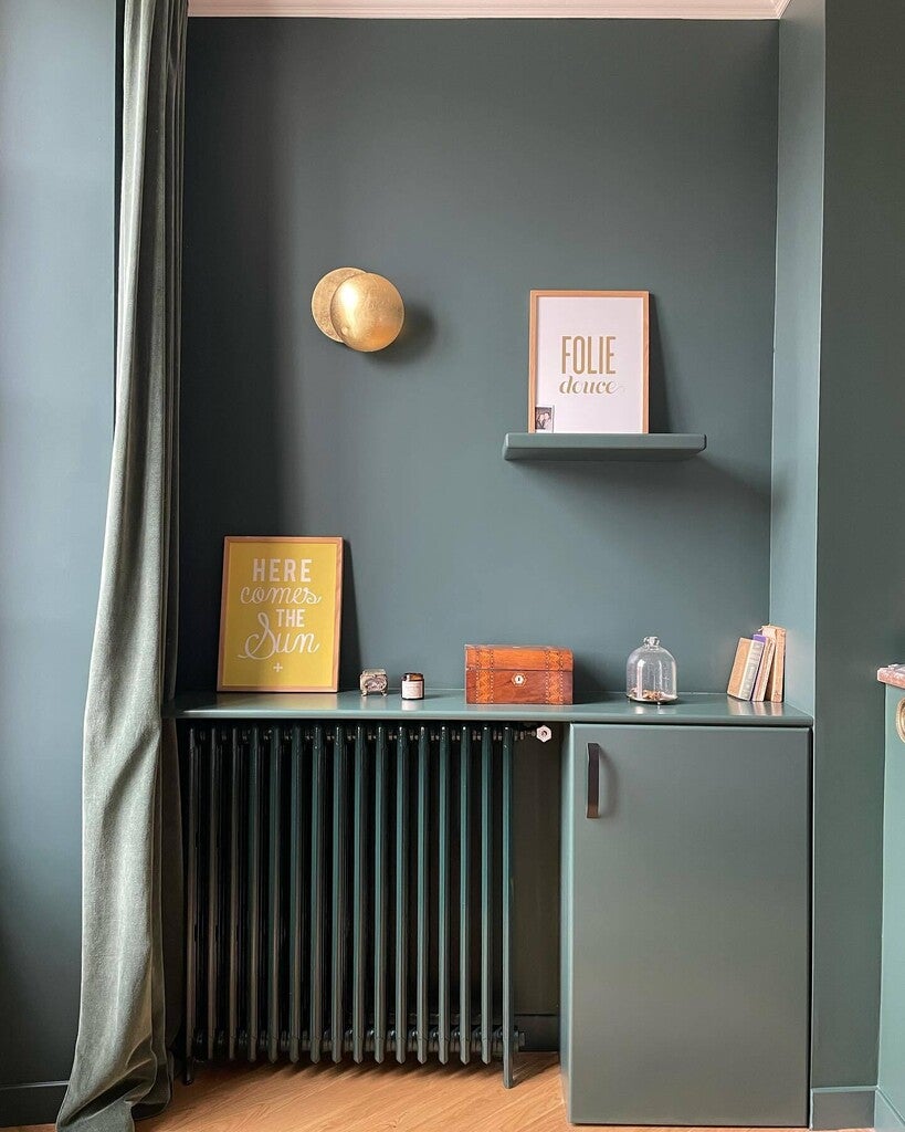 Nook with a shelf, wall sconce, and decorative items against a dark green wall.