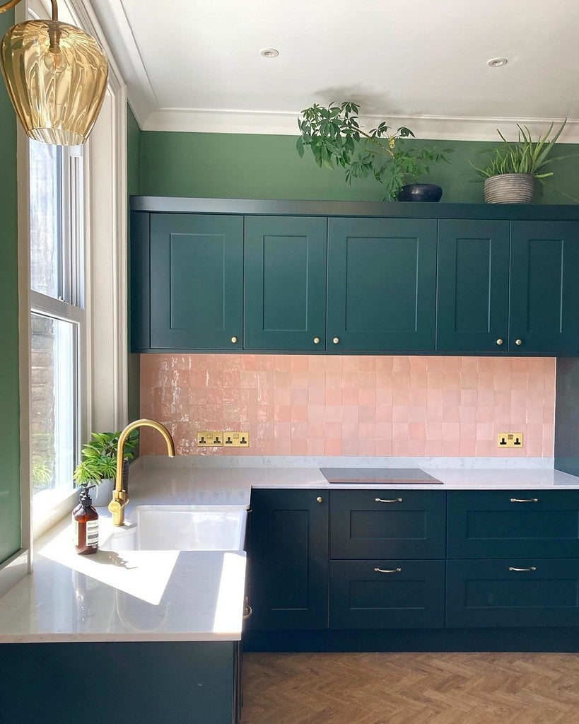 Modern kitchen with green cabinets, pink tiled backsplash, and gold fixtures.
