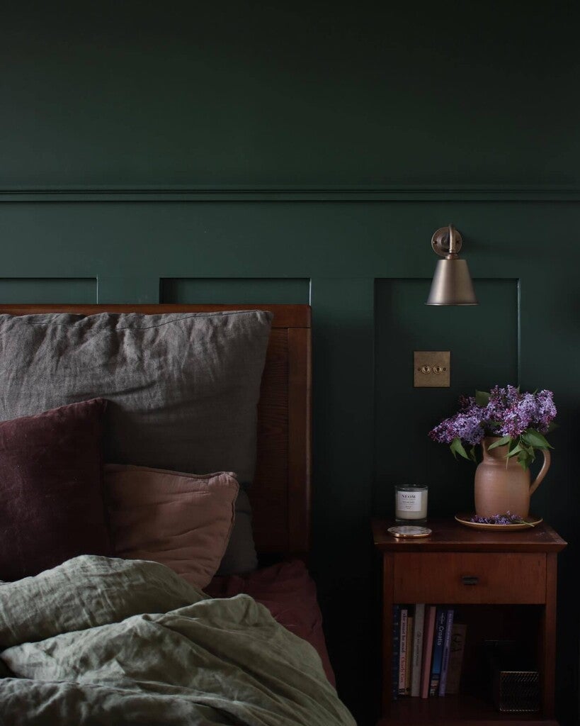 Dark green bedroom with a bed and nightstand featuring a lamp and vase.
