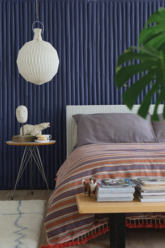 Modern bedroom with striped bedding, side table, and decorative elements against a dark blue wall.