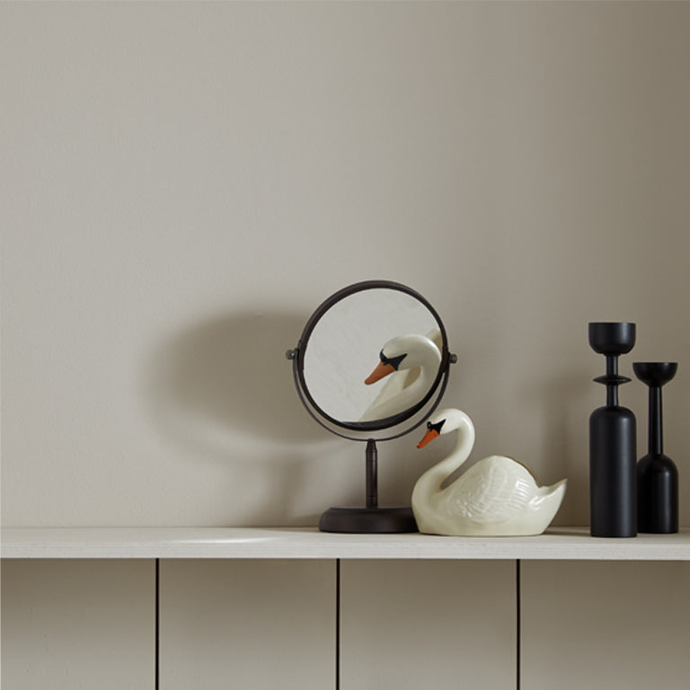 Decorative swan figure, round mirror, and black vases on a shelf against a beige wall.