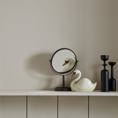 Decorative swan figure, round mirror, and black vases on a shelf against a beige wall.