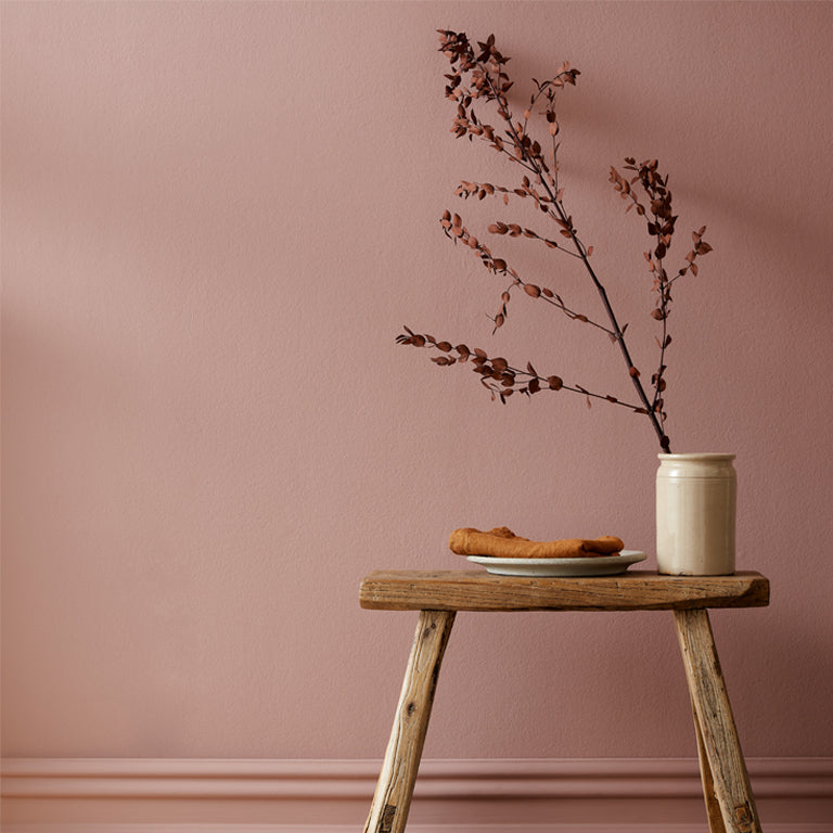 Wooden stool with a vase and branches against a pink wall
