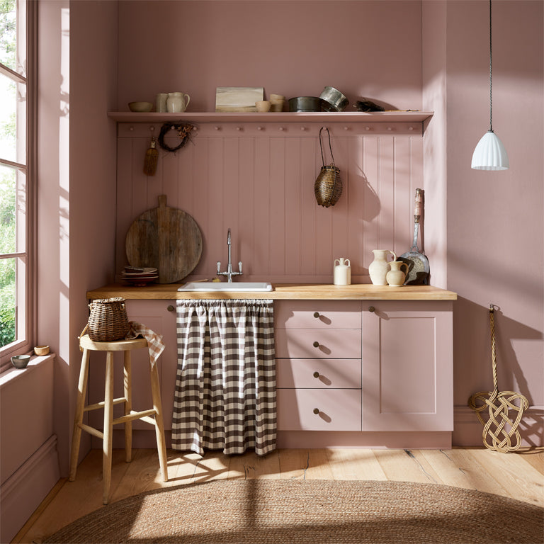 Pink kitchen with wooden counter, sink, and various kitchen items.