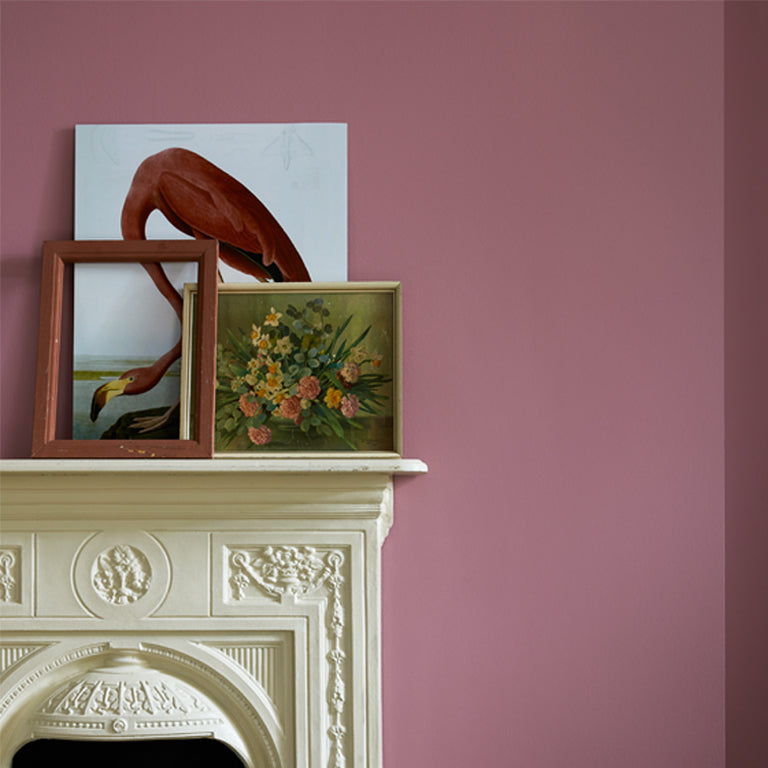 Framed artworks on a decorative fireplace against a pink wall