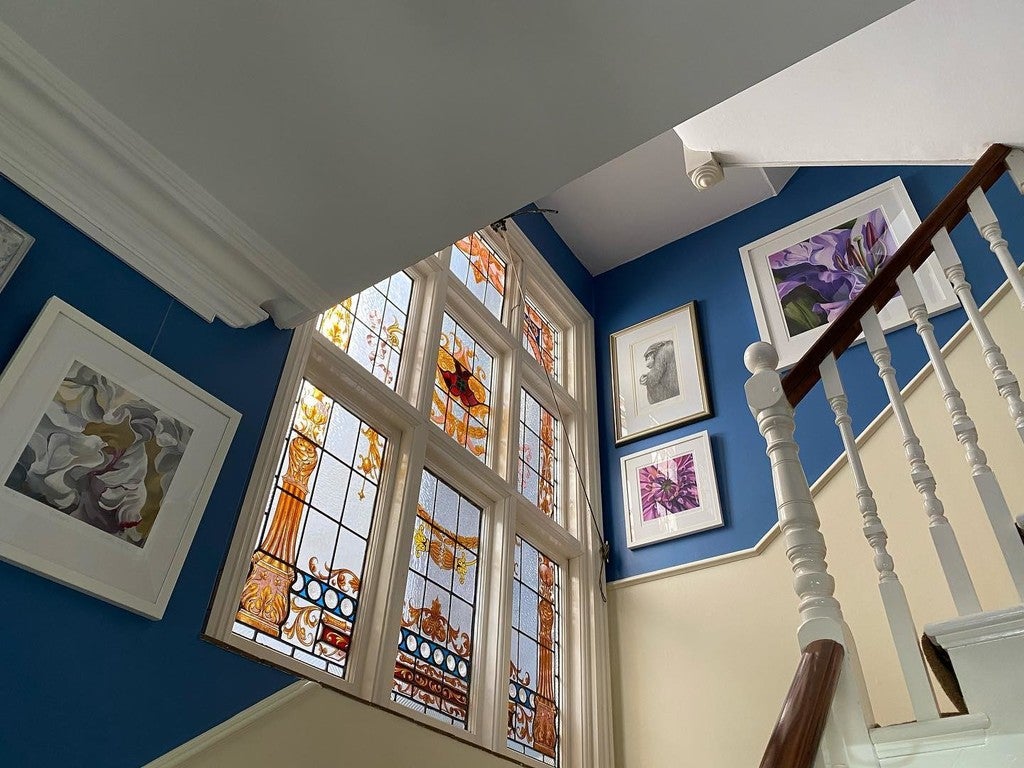 Staircase with stained glass window and framed pictures on a blue wall