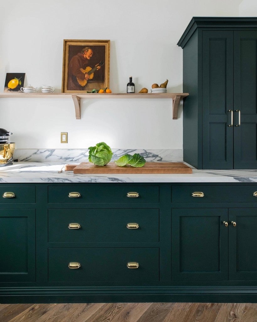Modern kitchen with dark green cabinets, marble countertop, and wooden flooring.