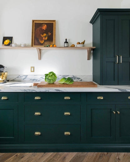 Modern kitchen with dark green cabinets, marble countertop, and wooden flooring.