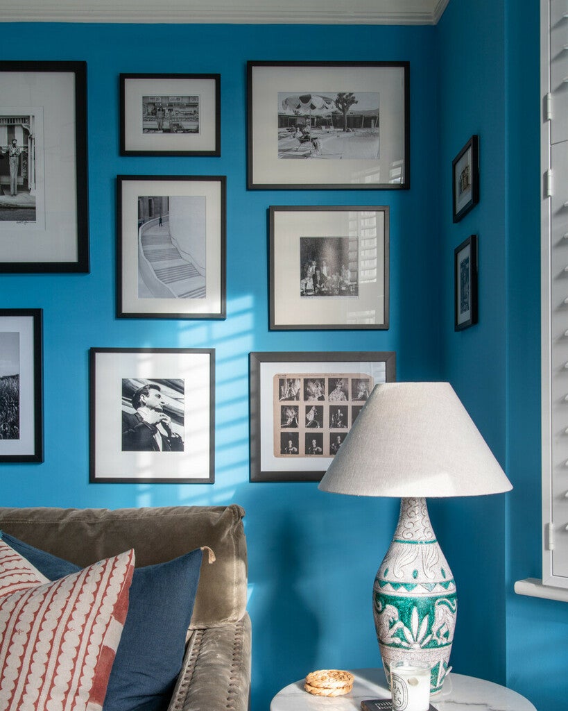 Blue wall with framed pictures and a lamp on a table.