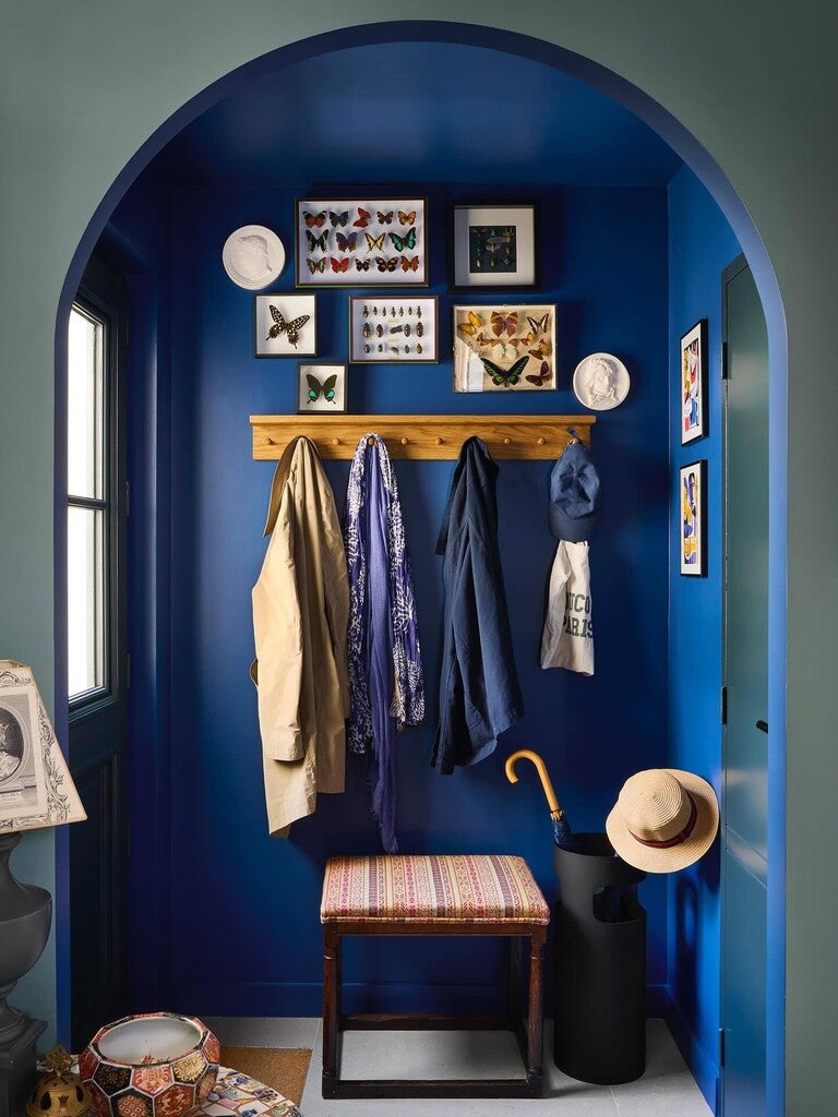 Nook with blue walls, wooden coat rack, and various items including coats, hats, and a stool.