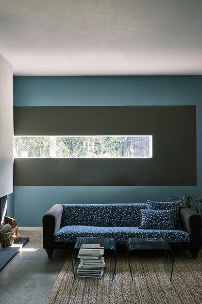 Modern living room with a blue sofa and decorative pillows against a teal wall.