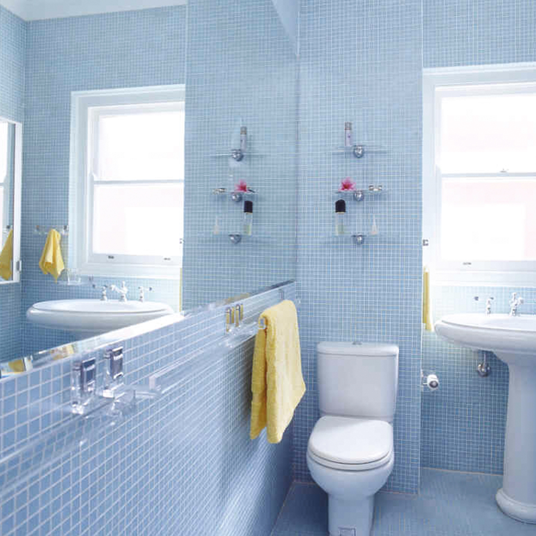 Bathroom with blue tiled walls, white toilet, and sink with yellow towel.