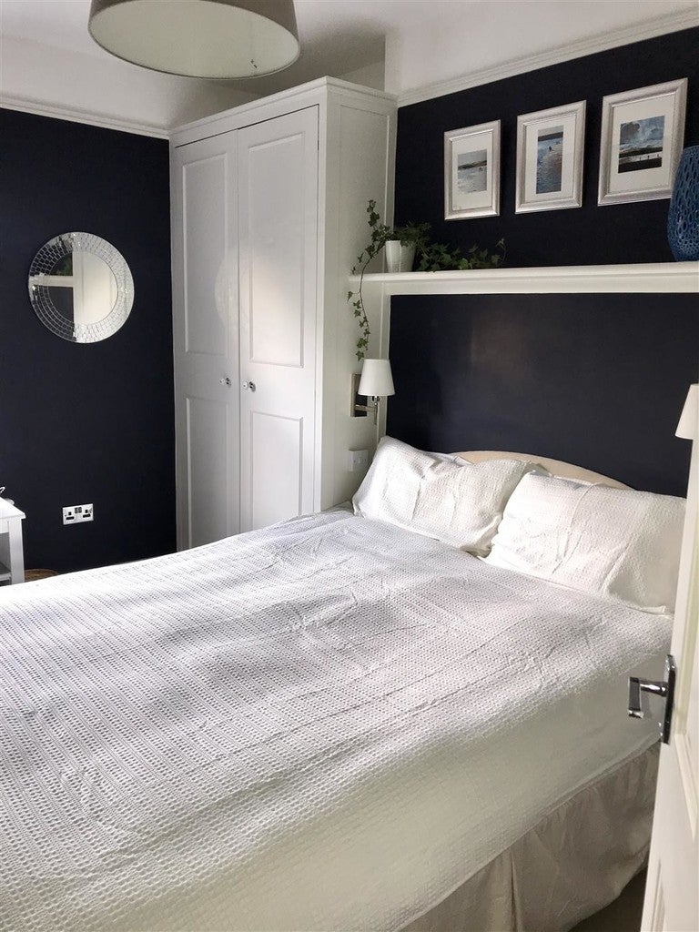 Modern bedroom with white bed, dark walls, and framed pictures.