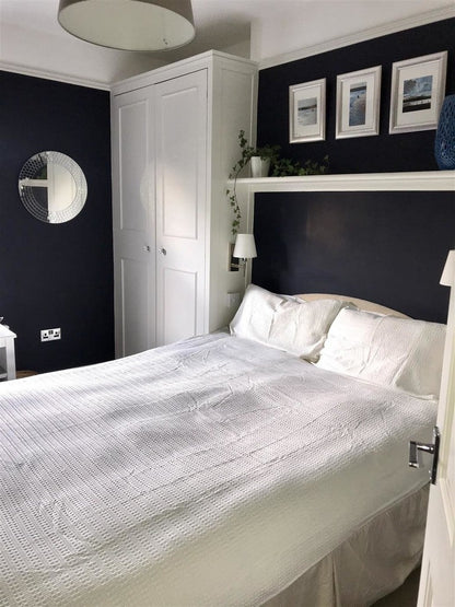 Modern bedroom with white bed, dark walls, and framed pictures.