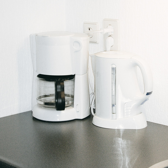 White coffee maker and kettle on a gray surface with a white wall background