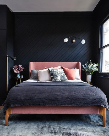 Pink bed with gray bedding in a bedroom with dark walls and decor.