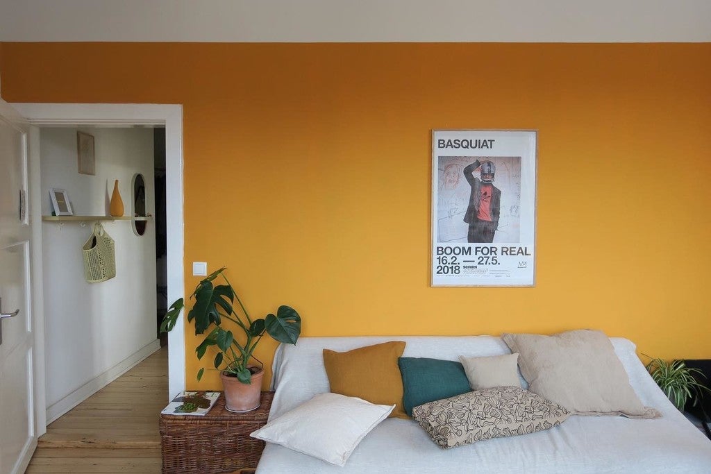 Living room with yellow wall, white sofa, and Basquiat poster.