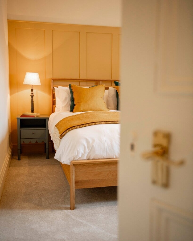 Bedroom with wooden bed and nightstand, lamp, and decorative pillows.