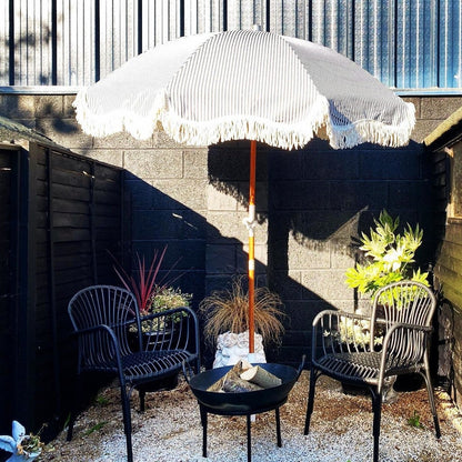 Outdoor setting with a white patio umbrella, two chairs, and a fire pit against a corrugated metal wall.