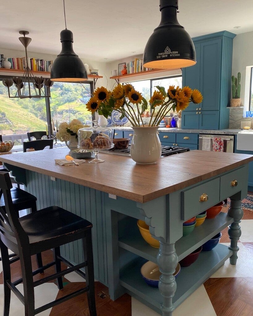 Kitchen island with wooden top and blue base, featuring a vase of sunflowers.