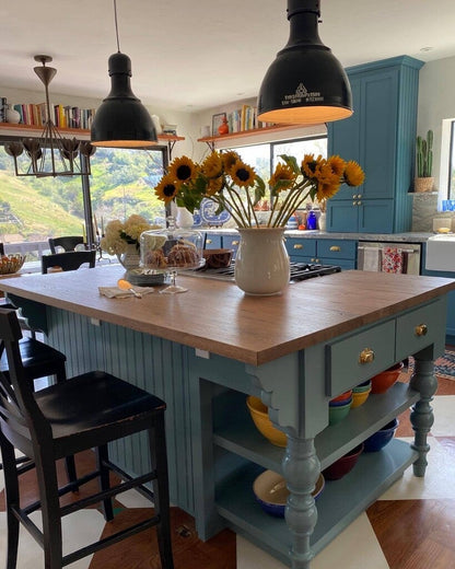 Kitchen island with wooden top and blue base, featuring a vase of sunflowers.