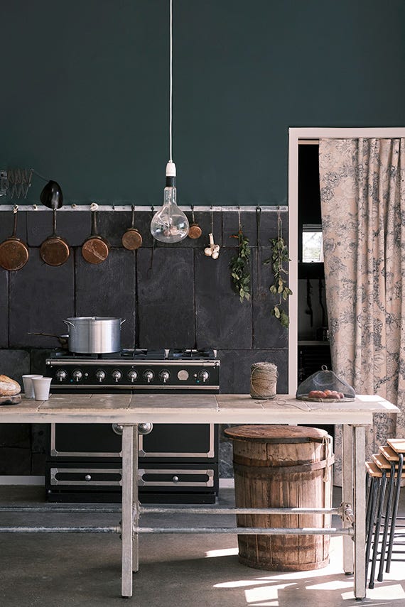 Kitchen interior with dark green walls, wooden table, and various kitchen items.