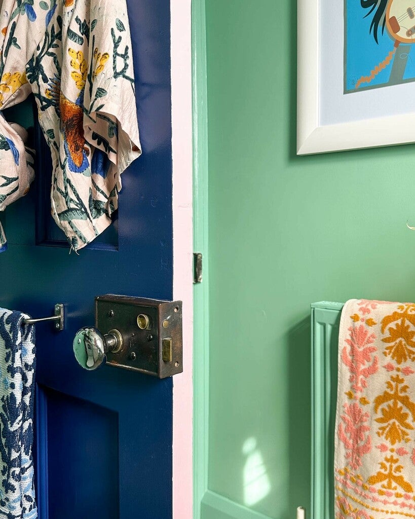 Close-up of a blue door with floral towels, a green wall, and a framed picture.