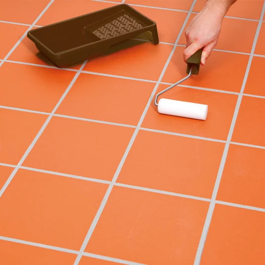 Person using a paint roller to apply orange paint on a tiled floor.
