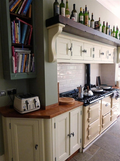 Kitchen with Aga range cooker, wooden countertop, and bookshelf.