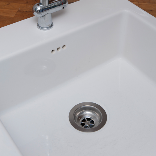 White kitchen sink with silver faucet on a wooden floor