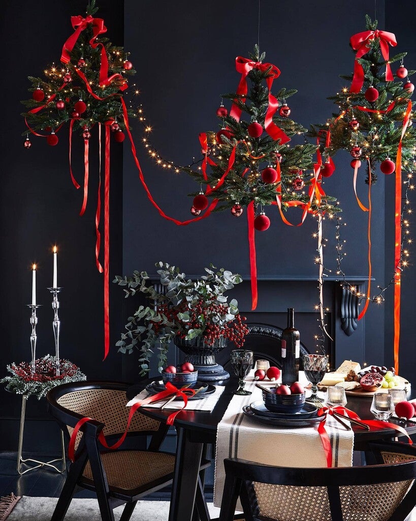 Decorative Christmas trees with red ribbons and lights hanging above a dining table set for a meal.
