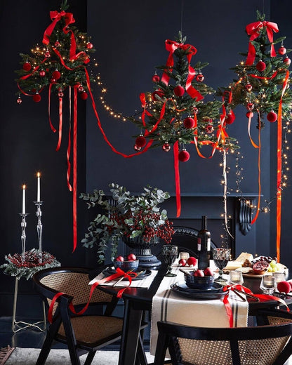 Decorative Christmas trees with red ribbons and lights hanging above a dining table set for a meal.