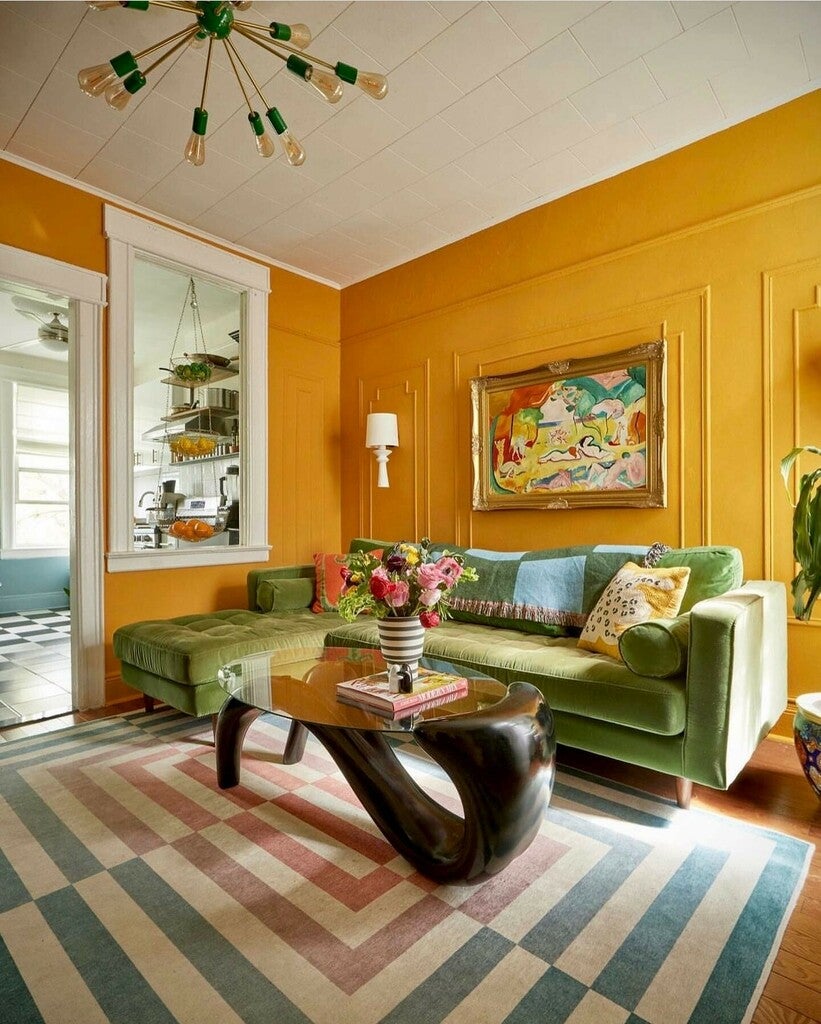 Living room with green sofa, colorful rug, and abstract painting on yellow wall