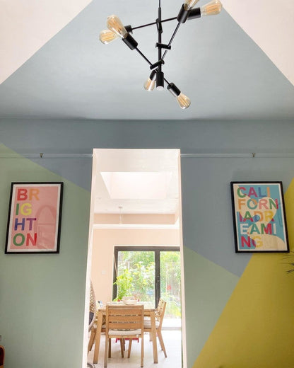 Modern chandelier hanging from a geometric ceiling with colorful wall art in a room.