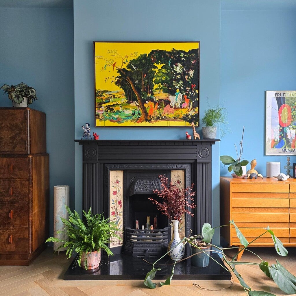 Living room with a fireplace, plants, and colorful artwork on a blue wall.