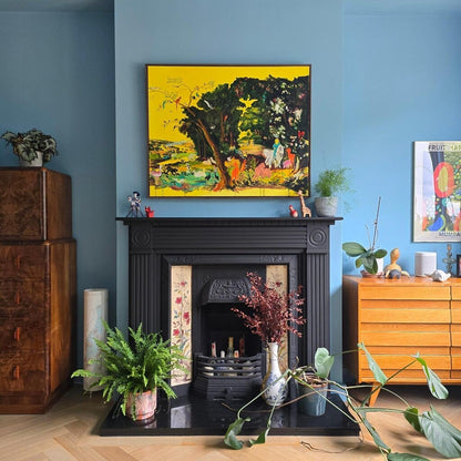 Living room with a fireplace, plants, and colorful artwork on a blue wall.
