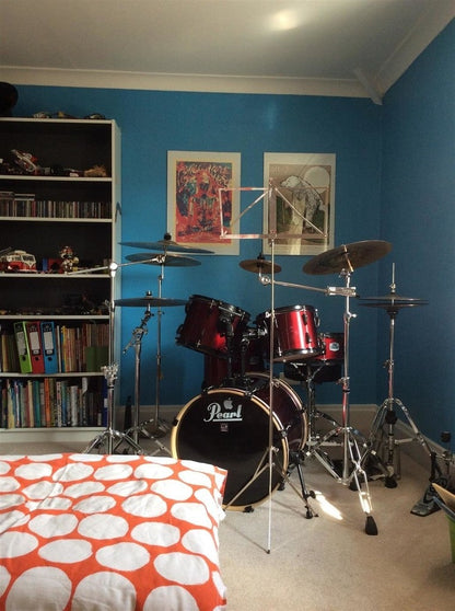 Drum set in a room with blue walls, bookshelf, and bed with red and white polka dot cover.