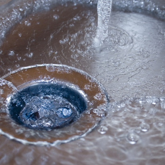 Close-up of water flowing into a sink drain with bubbles.