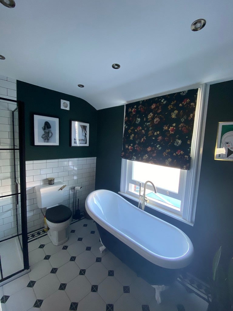 Bathroom with a freestanding bathtub, toilet, and window with floral curtain.