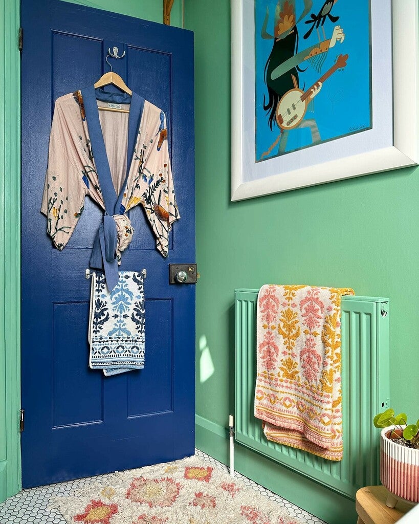 Blue door with hanging clothes, green radiator with a towel, and colorful artwork on a green wall.