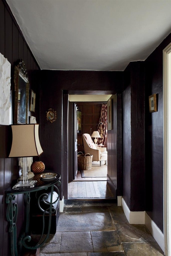 Dark hallway with a lamp on a side table and a room in the background.