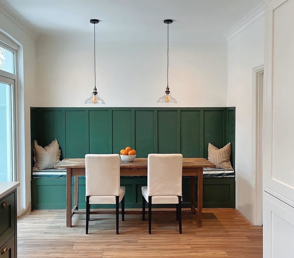 Dining area with a wooden table, white chairs, and green paneled wall.