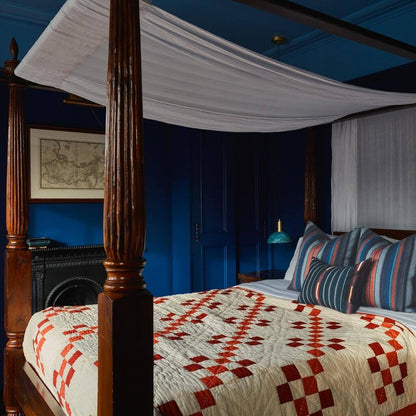 Bedroom with a four-poster bed featuring a patterned quilt and striped pillows against a blue wall.
