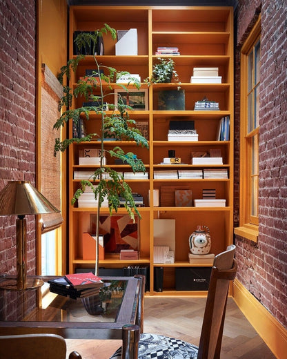 Wooden bookshelf filled with books and decorative items in a room with brick walls.