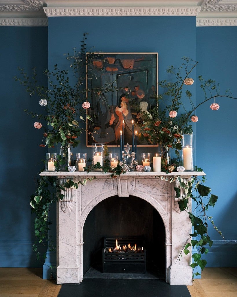 Decorative fireplace with candles, flowers, and a mirror against a blue wall.