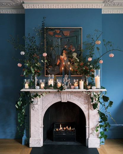 Decorative fireplace with candles, flowers, and a mirror against a blue wall.