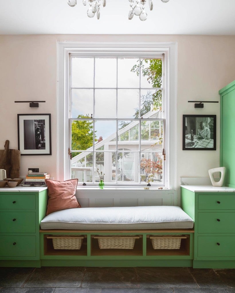 Green built-in bench with cushion in a room with large window and light-colored walls.